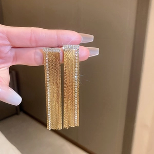 Macro shot of gold tassel drop earrings with sparkling rhinestones and letter details