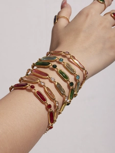 Detail of layered gold-plated bracelets featuring colorful rectangular glass gemstones