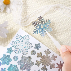 Close-up of sparkling snowflake stickers being applied with tweezers for holiday crafts