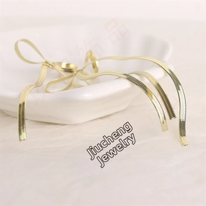 Detailed view of golden flat herringbone snake chain coiled on a white ceramic tray