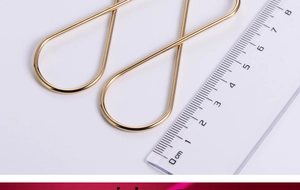Macro view of gold titanium steel figure-eight earrings with a ruler for scale