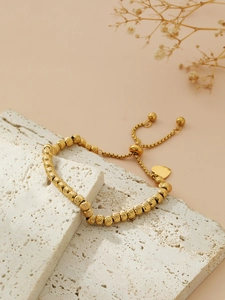 Close-up of gold beaded bracelet with heart charm on natural stone texture background