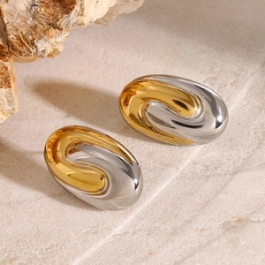 Macro shot of two-tone S-shaped curved earrings on textured beige stone surface