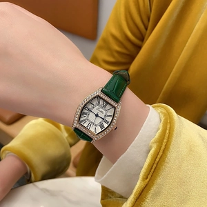 Close-up of women's gold tonneau watch with green leather strap and rhinestone bezel