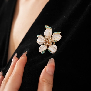 Gros plan d'une broche fleur blanche en émail avec perles turquoise sur un vêtement noir élégant