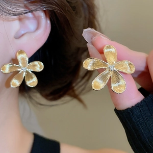 Dettaglio di orecchini a fiore in oro spazzolato con cristallo centrale e trama metallica