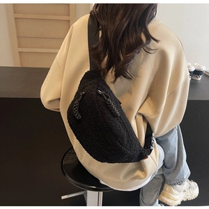 Detail of black fleece crossbody bag with woven zipper pull worn by a model in a cafe
