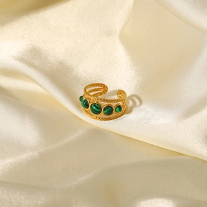 Close-up of gold open ring with four round green malachite stones on silk fabric