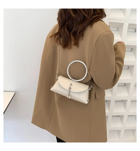 Detail of a creamy white handbag with a sparkling rhinestone ring handle and metal chain