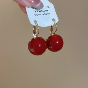 Macro detail of red resin beaded earrings with gold plated hoops and silver hallmark tag