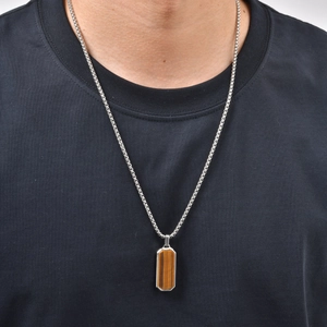 Detail einer Edelstahlkette mit rechteckigem Tigerauge-Anhänger getragen auf schwarzem Shirt