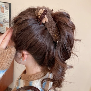 Detailed view of a brown plush bear hair tie with a bow on a braided hairstyle