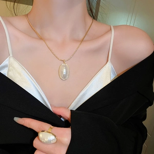 Détail d'un ensemble collier et bague en perles ovales dorées porté avec élégance