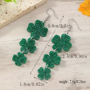 Detailed view of green glitter shamrock earrings showing dimensions 9.0cm long on wood