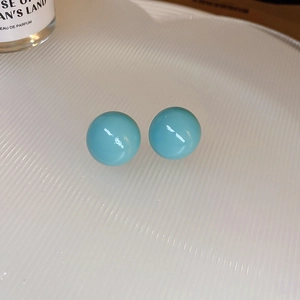 Gros plan de boucles d'oreilles rondes bleu ciel sur une assiette blanche texturée