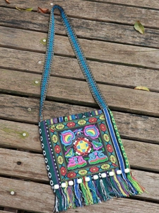 Ethnic style embroidered crossbody bag with colorful tassels and bead charms on wood floor