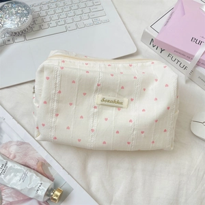 Close-up of a cream canvas makeup bag featuring pink heart patterns and zipper detail