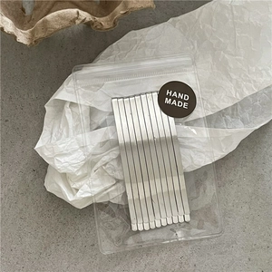 Set of ten silver metal hair clips in transparent handmade packaging on a textured background