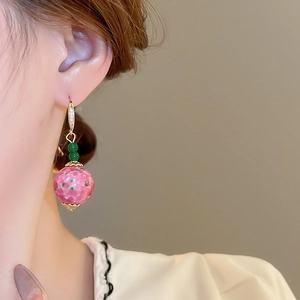 Macro shot of ceramic pink ball earrings with green dots and gold stud details