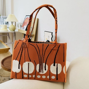 Close-up of orange knit tote bag featuring black lines and white polka dots on a sofa