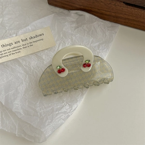Close-up of a handbag-shaped hair claw clip with checkered pattern and cherry rhinestones