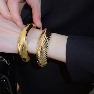 Gros plan d'un bracelet ovale doré poli et d'une manchette texturée sur le poignet d'un mannequin