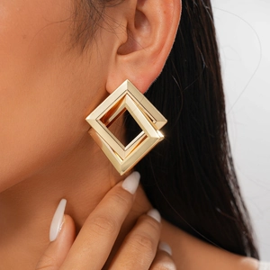 Close-up of golden geometric square earrings worn by a model showing luxury metallic texture