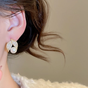 Detail of elegant gold-plated pearl stud earring with sparkling zircon leaf on ear lobe