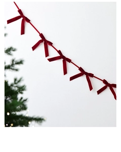 Close-up of a red velvet Christmas bow decoration hanging on a white wall for festive party
