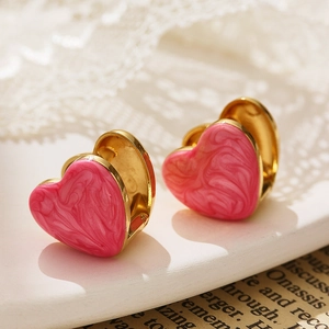 Gros plan de boucles d'oreilles cœur dorées avec émail marbre rose sur dentelle