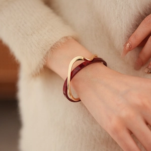 Detail of layered gold wave bracelet and burgundy marble bangle on soft knit sweater
