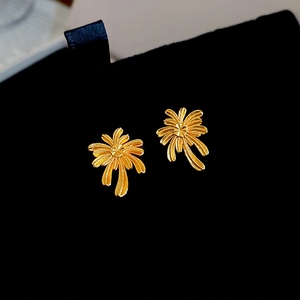 Macro shot of gold-plated palm tree stud earrings on a premium black velvet background