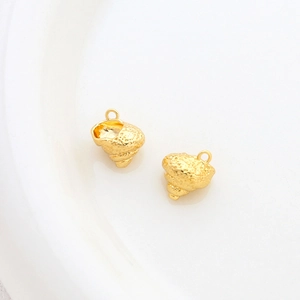 Macro shot of 14k gold-plated conch shell pendants with textured metal finish on white ceramic