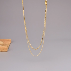 Golden multi-layer necklace with figaro chain and slim flat chain on neutral background