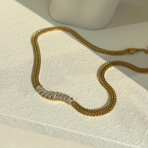 Macro detail of gold Cuban chain necklace featuring baguette-cut zircon stones on a white stand