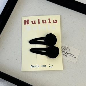 Detail of two black velvet rose hair clips mounted on a branded display card