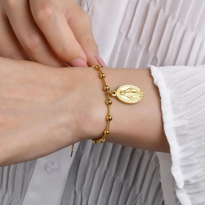 Gold beaded rosary bracelet with oval Virgin Mary medallion on woman's wrist