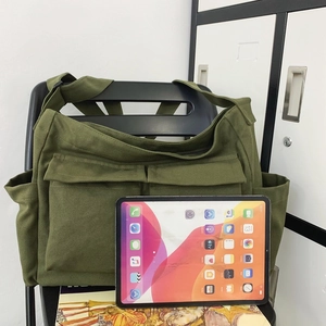 Green canvas shoulder bag with multi-pocket workwear design and tablet for size scale