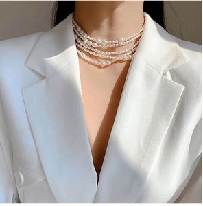 Detail of layered freshwater pearl necklace with gold chain on model in white suit