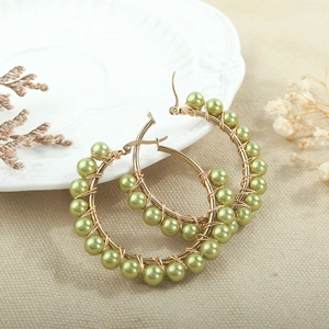 Close-up of handmade gold wire hoop earrings with pale green pearls on a ceramic plate