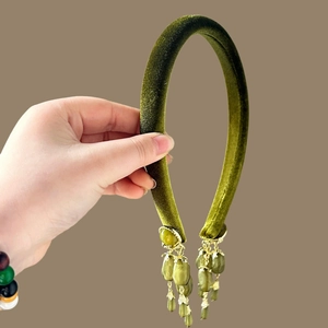 Détail d'un serre-tête en velours vert émeraude avec des pendentifs à pompons dorés