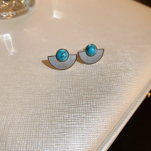 Macro detail of fan-shaped silver earrings with turquoise inlay on white leather