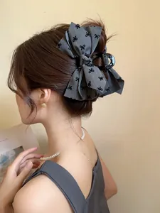 Dettaglio di un fermaglio per capelli a fiocco grigio con stampe nere su un modello