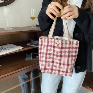 Close-up of a person holding a red plaid wool handbag in a cozy indoor setting