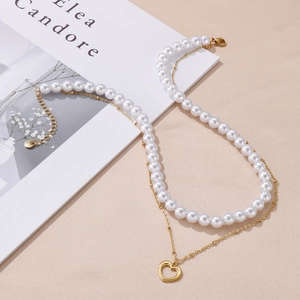 Detail of double-layer necklace with white pearls and gold heart pendant on pink background