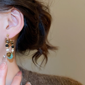 Detail of vintage beaded earrings with tiger eye, pearls, and light blue stone on model