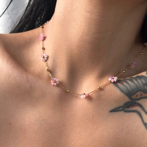 Detailed close-up of a gold necklace with pink and white floral beads on a model neck