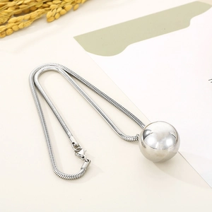 Close-up of a silver-toned snake chain necklace featuring a large polished metal ball pendant