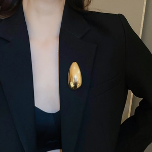 Close-up of polished golden teardrop brooch pinned on a black suit jacket lapel