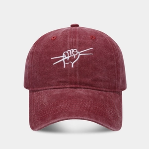 Close-up of a burgundy washed denim baseball cap with white fist embroidery and vintage texture